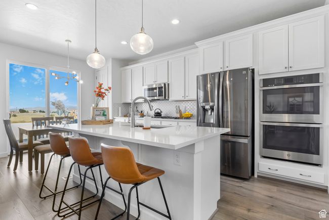 Kitchen with backsplash, appliances with stainless steel finishes, a sink, an island with sink, and wood finished floors | Image 27