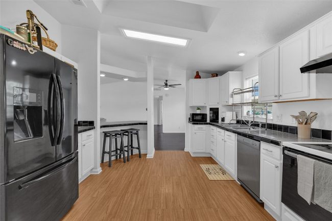 Kitchen featuring black appliances, white cabinetry, light wood-style flooring, dark countertops, and recessed lighting | Image 12