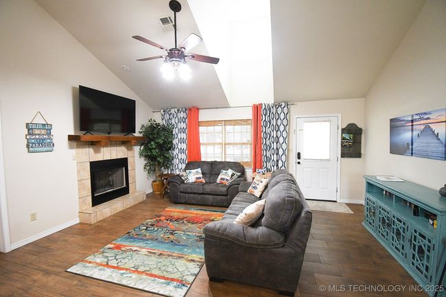 Living area with ceiling fan, wood finished floors, high vaulted ceiling, baseboards, and a tiled fireplace | Image 5