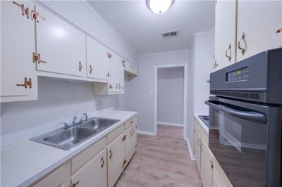 Kitchen with white cabinets, oven, light wood-type flooring, sink, and ornamental molding | Image 3