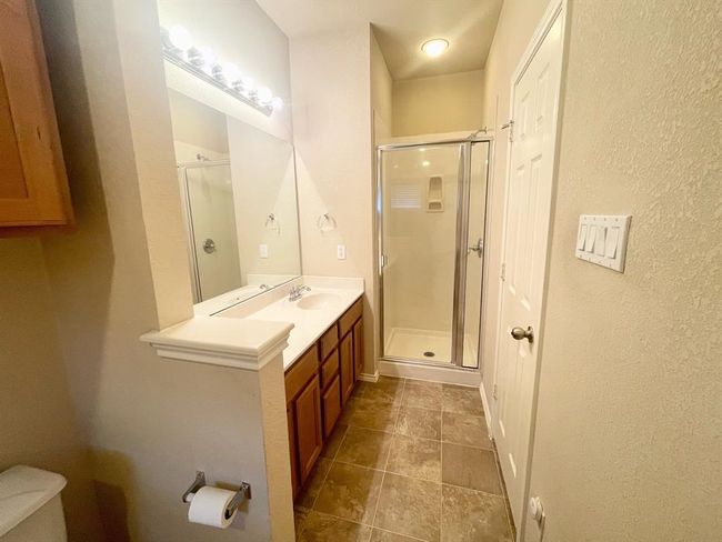 Bathroom with a stall shower, toilet, vanity, tile patterned floors, and a textured wall | Image 13