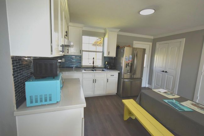 Modern kitchen with sleek stainless steel appliances, white cabinetry, and a stylish blue tile backsplash. Features ample natural light and a functional layout. | Image 9