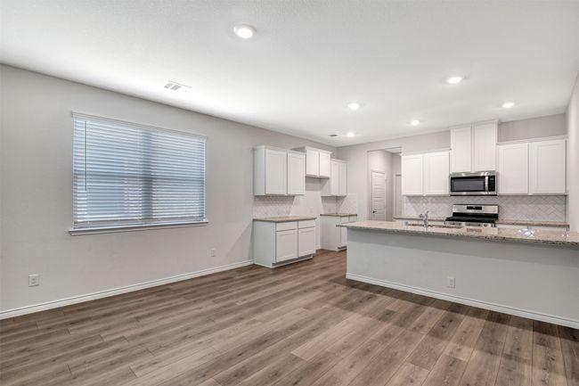 Kitchen with appliances with stainless steel finishes, backsplash, wood finished floors, white cabinets, and recessed lighting | Image 7