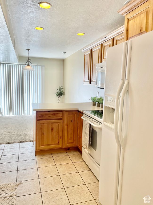 Kitchen featuring white appliances, a peninsula, light tile patterned floors, a textured ceiling, and light countertops | Image 10