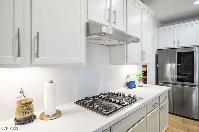 Kitchen featuring under cabinet range hood, light wood-style flooring, light countertops, white cabinets, and appliances with stainless steel finishes | Image 16