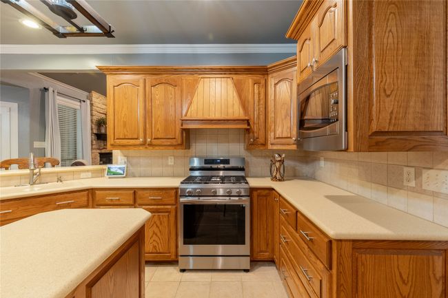 Kitchen featuring appliances with stainless steel finishes, custom exhaust hood, crown molding, light countertops, and brown cabinets | Image 15