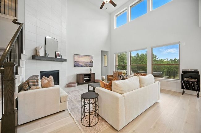 Living area featuring a towering ceiling, ceiling fan, wood finished floors, and a tile fireplace | Image 5