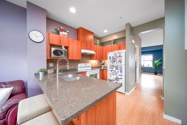Kitchen with brown cabinets, under cabinet range hood, a sink, white appliances, and a peninsula | Image 16