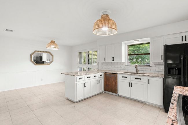 Kitchen with black appliances, a peninsula, white cabinetry, and plenty of natural light | Image 13