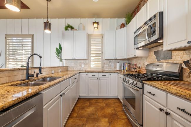 Kitchen featuring decorative backsplash, white cabinets, stainless steel appliances, a sink, and pendant lighting | Image 12