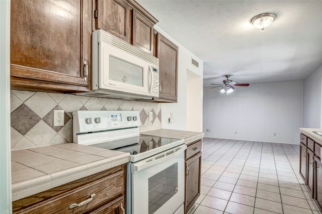 Kitchen featuring white appliances, decorative backsplash, ceiling fan, tile counters, and light tile patterned floors | Image 12