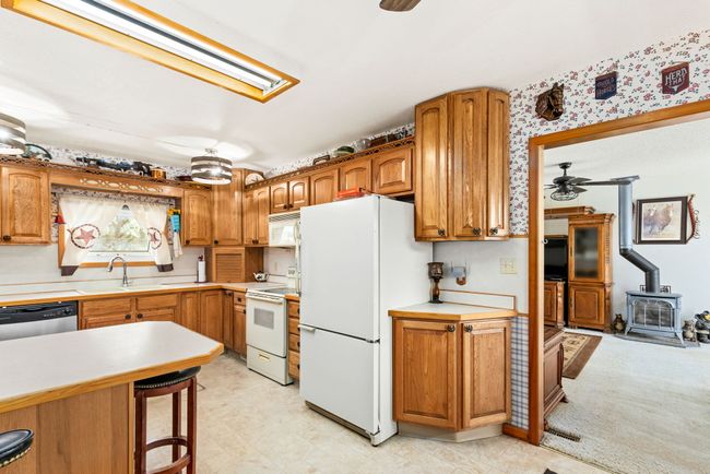 Kitchen with light countertops, white appliances, a breakfast bar, ceiling fan, and a wood stove | Image 43