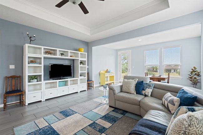 Living room with a tray ceiling, a ceiling fan, ornamental molding, and baseboards. | Image 9