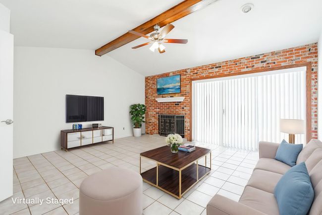 Living area featuring ceiling fan, vaulted ceiling with beams, tile patterned flooring, and a brick fireplace | Image 21
