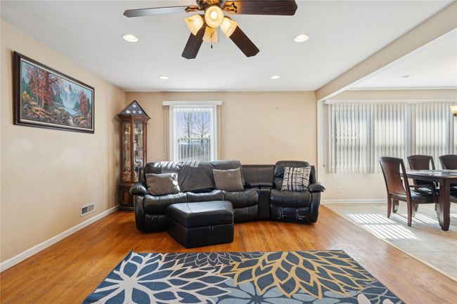 Living area with a ceiling fan, wood finished floors, visible vents, and baseboards | Image 15