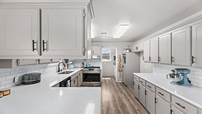 Kitchen featuring stainless steel range with gas stovetop, tasteful backsplash, black dishwasher, a sink, and fridge | Image 39
