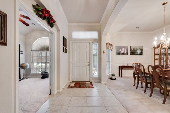 Carpeted foyer featuring ornamental molding, a chandelier, tile patterned flooring, baseboards, and arched walkways | Image 7