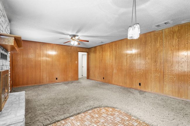 Unfurnished living room with a brick fireplace, ceiling fan, carpet flooring, wooden walls, and a textured ceiling | Image 12