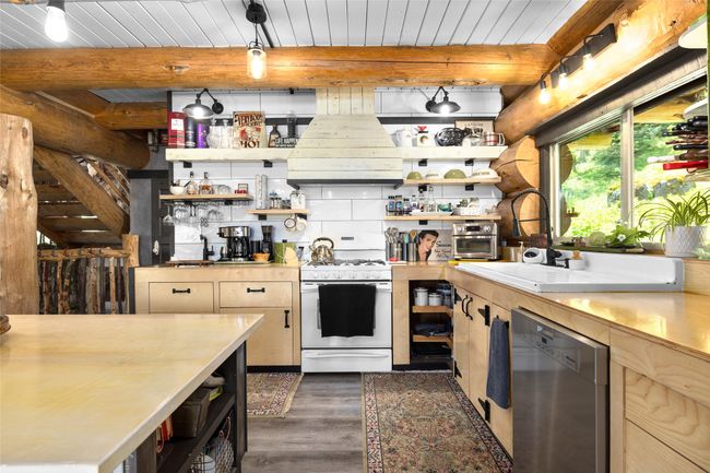 Kitchen with white gas range, stainless steel dishwasher, open shelves, premium range hood, and dark wood-style flooring | Image 5