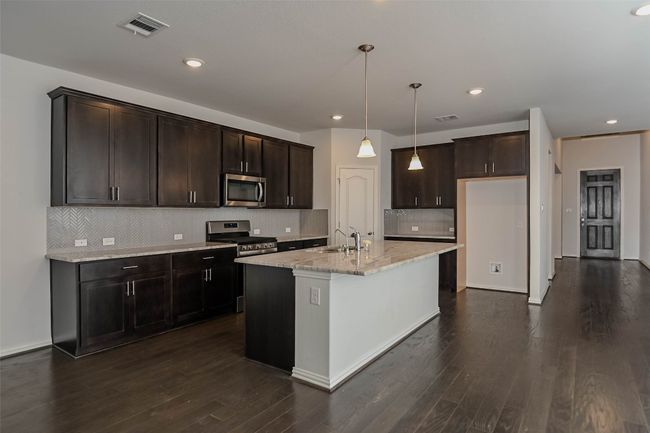 Kitchen featuring dark wood finished floors, appliances with stainless steel finishes, light stone counters, and visible vents | Image 12
