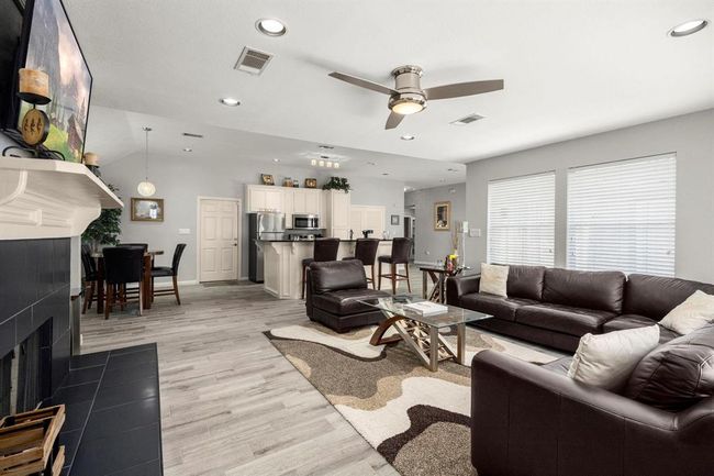 This is a modern, open-plan living space featuring a comfortable seating area with a dark leather sofa set. A sleek fireplace, a dining area, and a kitchen with stainless steel appliances. The room is well-lit with natural light from large windows, complemented by sophisticated neutral tones and wood flooring. | Image 35