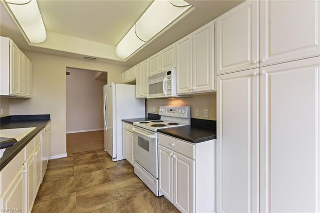 Kitchen with visible vents, white appliances, baseboards, dark countertops, and white cabinetry | Image 20
