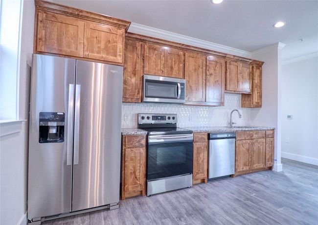 Kitchen featuring appliances with stainless steel finishes, sink, decorative backsplash, crown molding, and light wood-type flooring | Image 8