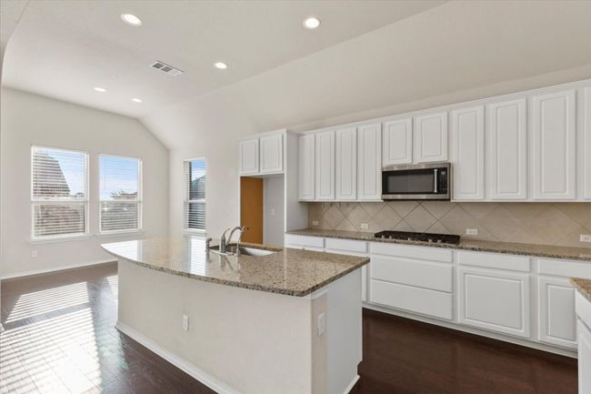 Kitchen with light stone countertops, white cabinetry, a kitchen island with sink, recessed lighting, and decorative backsplash | Image 8