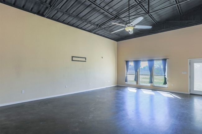 Empty room with a high ceiling, concrete floors, a ceiling fan, and baseboards | Image 5