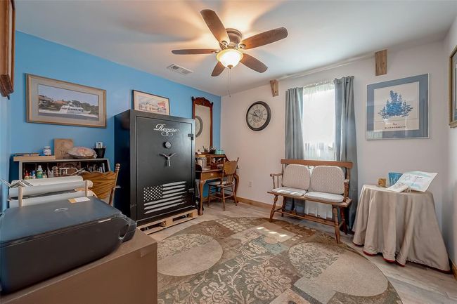 Bright and playful, this room features bright blue walls, a large window, and a ceiling fan. The charming wood door and neutral flooring provide a grounding contrast. | Image 19
