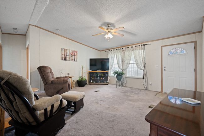 Living area with crown molding, ceiling fan, carpet, vaulted ceiling, and a textured ceiling | Image 7