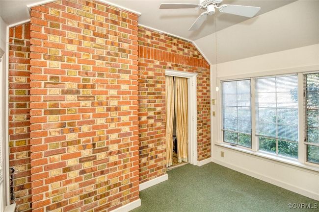 Unfurnished room with dark colored carpet, baseboards, vaulted ceiling, brick wall, and ceiling fan | Image 16