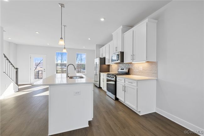 Kitchen featuring an island with sink, white cabinetry, dark wood finished floors, backsplash, and stainless steel appliances | Image 9