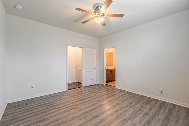 Unfurnished bedroom with wood finished floors, baseboards, ensuite bathroom, and a ceiling fan | Image 18