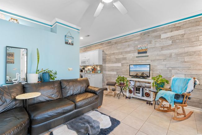Living area with wood walls, light tile patterned floors, ceiling fan, and lofted ceiling | Image 6