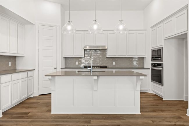 Kitchen featuring stainless steel oven, dark wood finished floors, under cabinet range hood, built in microwave, and a kitchen island with sink | Image 7