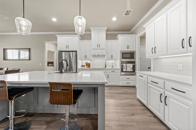 Kitchen with light wood-type flooring, a breakfast bar, visible vents, stainless steel appliances, and a sink | Image 6
