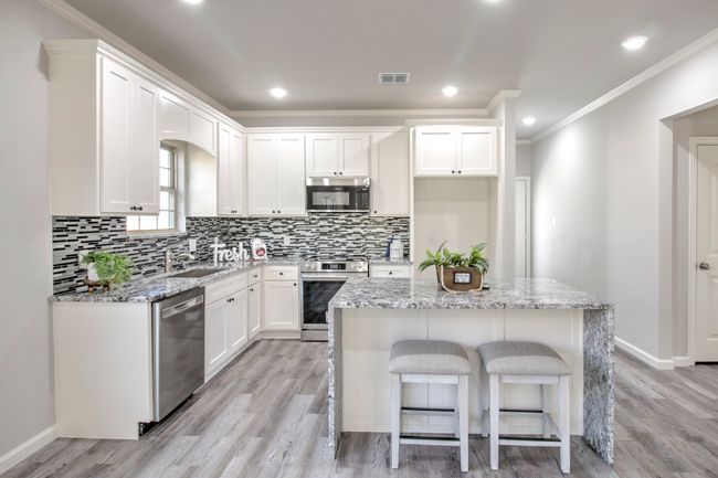 Kitchen with appliances with stainless steel finishes, crown molding, backsplash, light wood finished floors, and white cabinets | Image 7