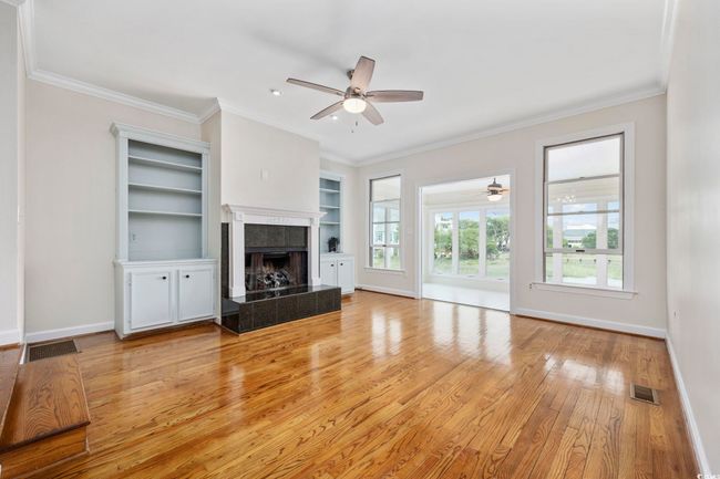 Unfurnished living room featuring a ceiling fan, baseboards, light wood-style floors, a tile fireplace, and ornamental molding | Image 10