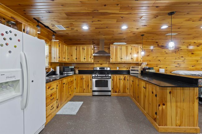 Kitchen featuring white refrigerator with ice dispenser, stainless steel gas stove, range hood, dark countertops, and a sink | Image 30