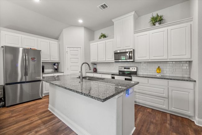 Kitchen featuring white cabinets, dark wood finished floors, decorative backsplash, and dark stone countertops | Image 8