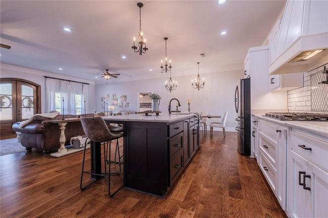 Kitchen featuring pendant lighting, white cabinets, ceiling fan with notable chandelier, a center island with sink, and dark hardwood / wood-style floors | Image 11