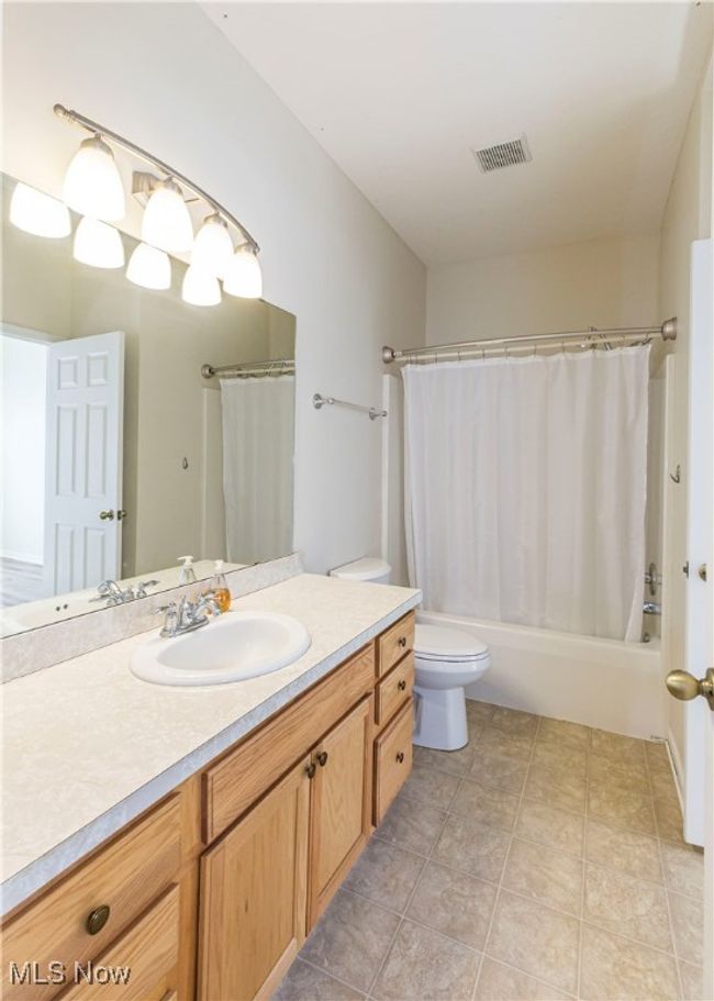 Bathroom featuring visible vents, toilet, tile patterned flooring, shower / bathtub combination with curtain, and vanity | Image 8