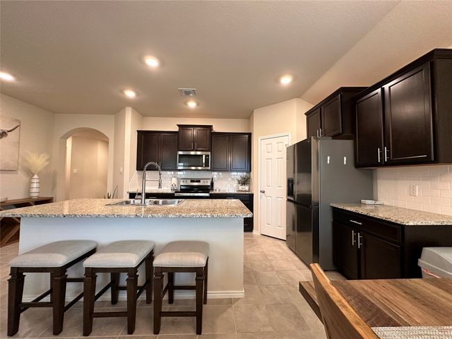 Kitchen with stainless steel appliances, a sink, arched walkways, decorative backsplash, and light stone counters | Image 22