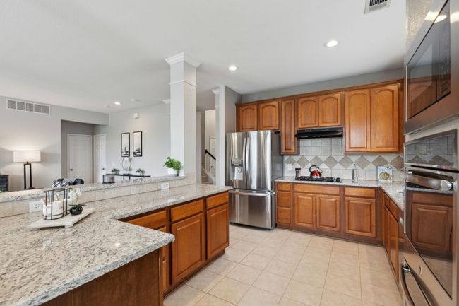 Kitchen featuring appliances with stainless steel finishes, light stone counters, decorative backsplash, light tile patterned floors, and under cabinet range hood | Image 7