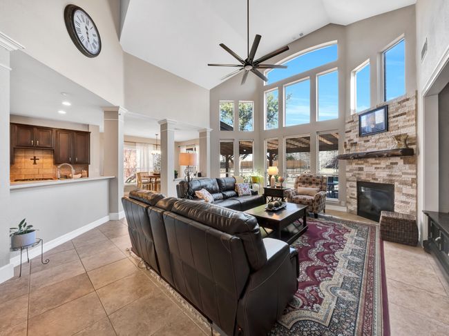 Family room with tile floors, a stone fireplace, ceiling fan, baseboards, and ornate columns | Image 20