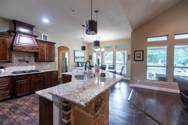 Kitchen featuring a sink, black gas cooktop, arched walkways, tasteful backsplash, and an island with sink | Image 17