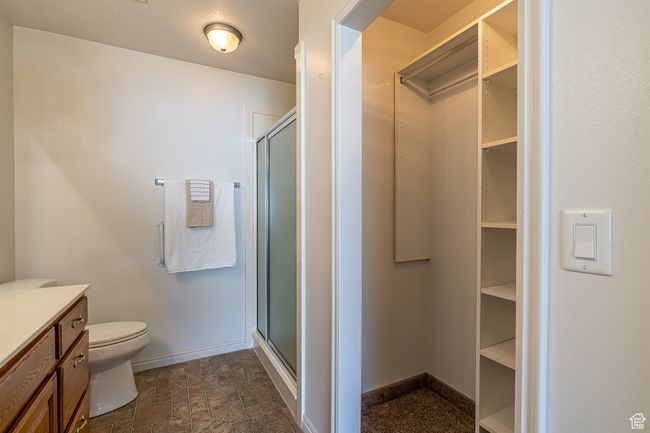 Full bathroom with a stall shower, toilet, a walk in closet, stone finish floor, and baseboards | Image 17