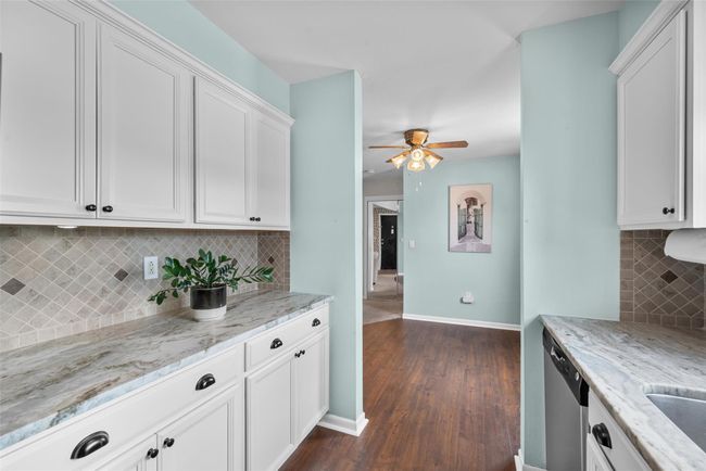 Kitchen with a ceiling fan, dark wood finished floors, backsplash, white cabinetry, and dishwasher | Image 16