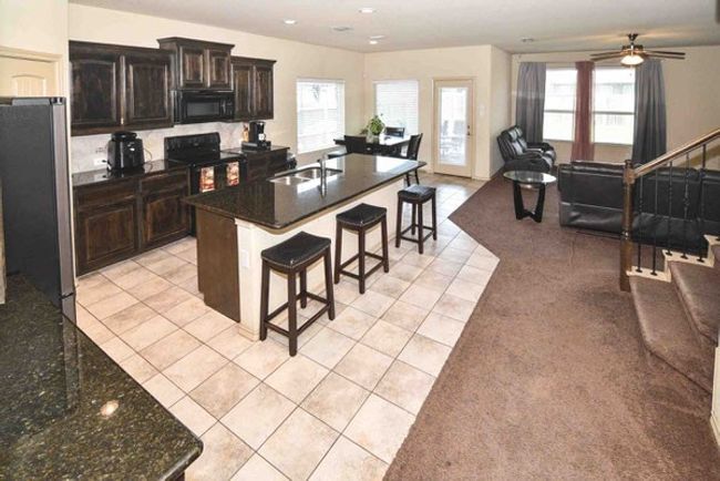Kitchen with black appliances, open floor plan, a kitchen breakfast bar, light tile patterned floors, and a sink | Image 7